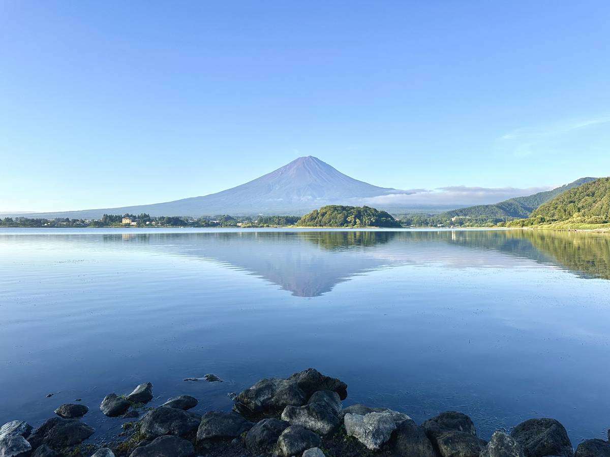 Mount Fuji reflecting in a still lake under a clear sky.
