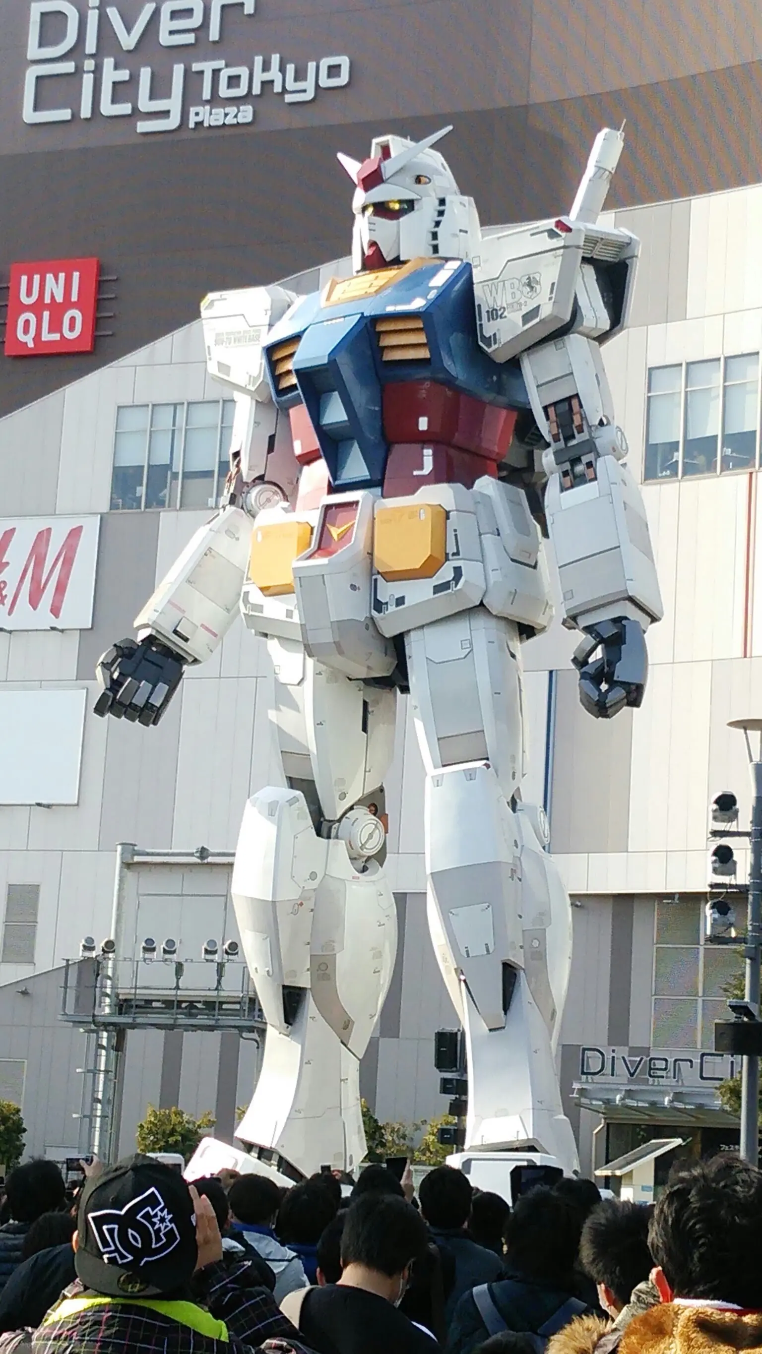 Gundam statue in front of Diver City Tokyo Plaza, surrounded by a crowd.