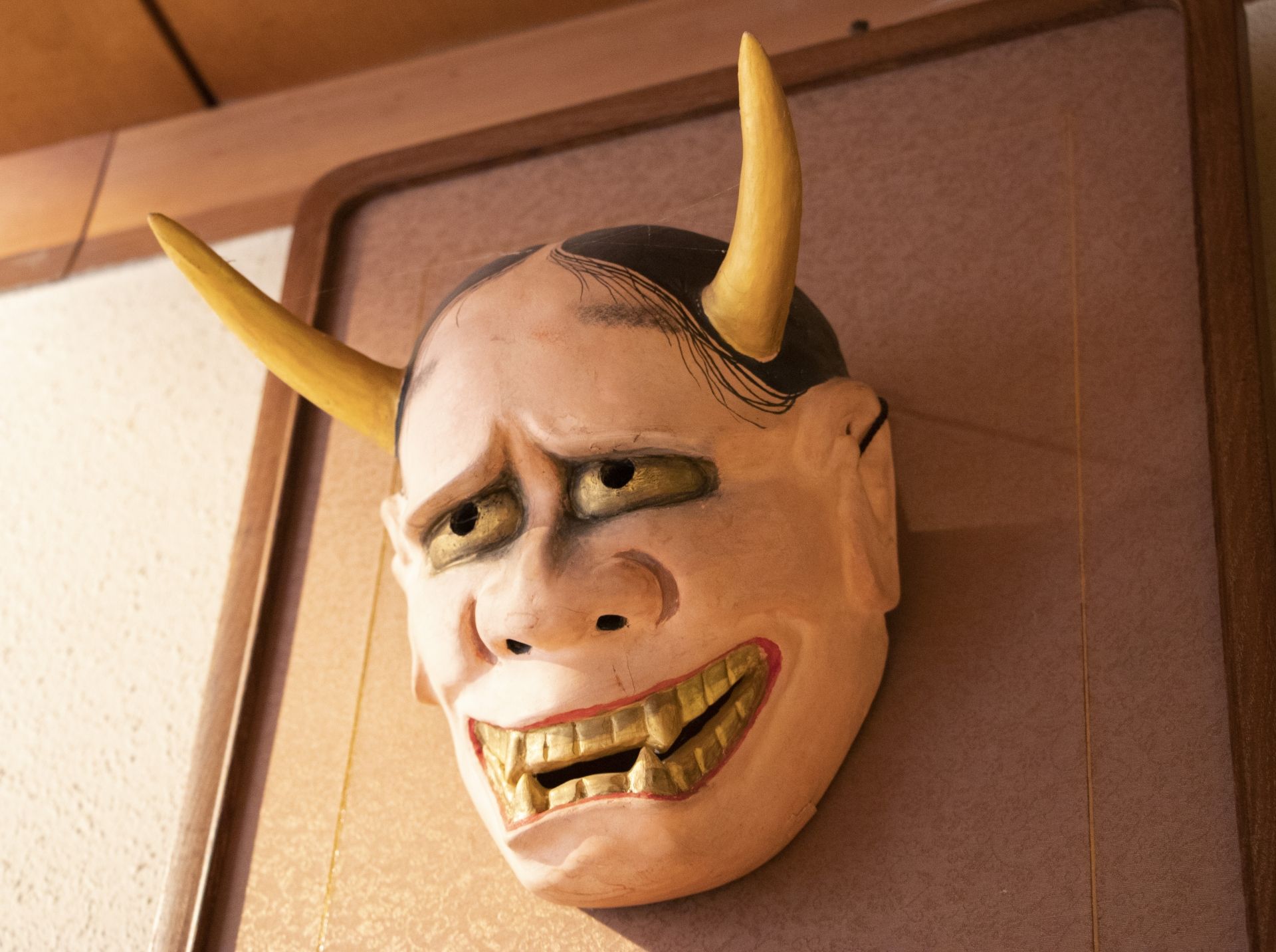 Traditional Japanese Hannya mask with yellow horns and a wide, toothy grimace.