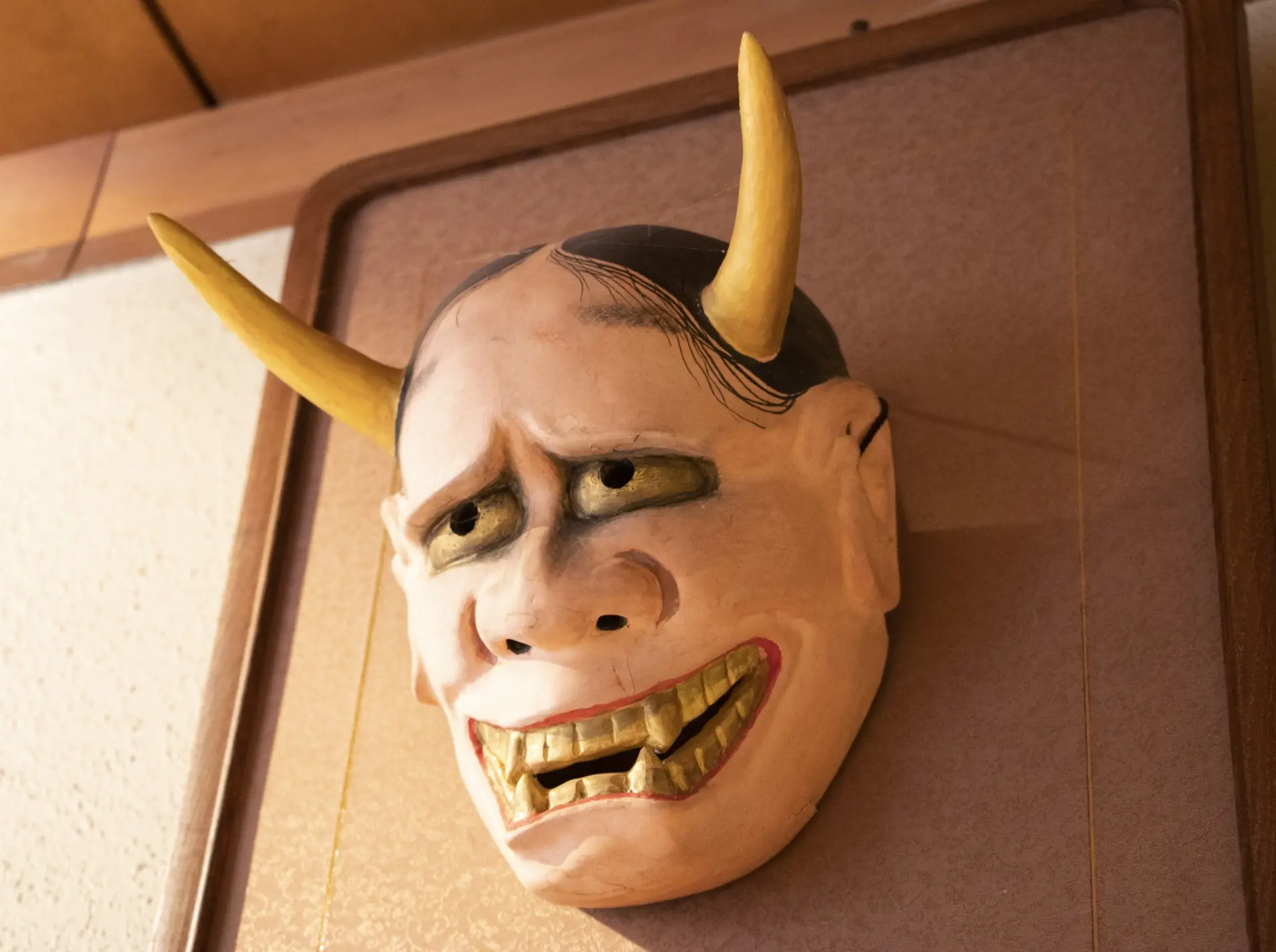Traditional Japanese Hannya mask with yellow horns and a wide, toothy grimace.