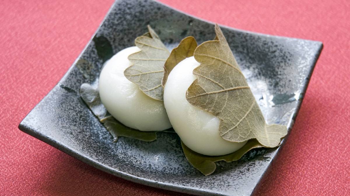 Two white, leaf-wrapped rice cakes on a dark plate.
