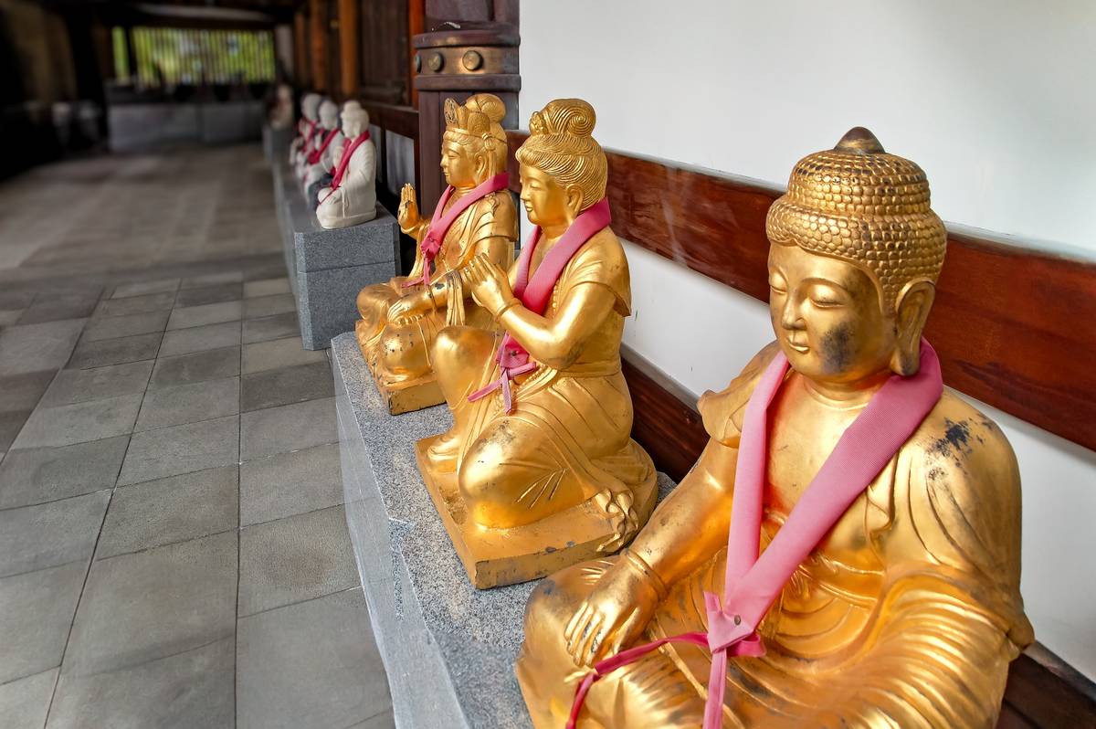 A row of golden statues with pink sashes, seated on a stone ledge.