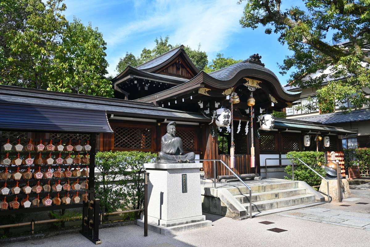 Traditional Japanese shrine with a seated bronze statue and a display of wooden ema tablets.