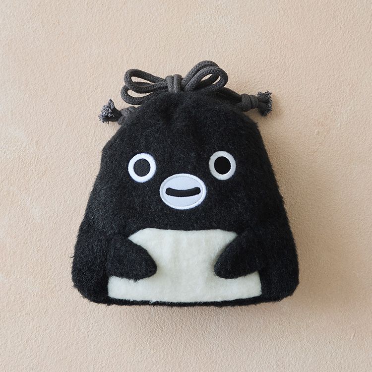 A fluffy black penguin-shaped drawstring pouch with white eyes, mouth, and belly, on a beige background.