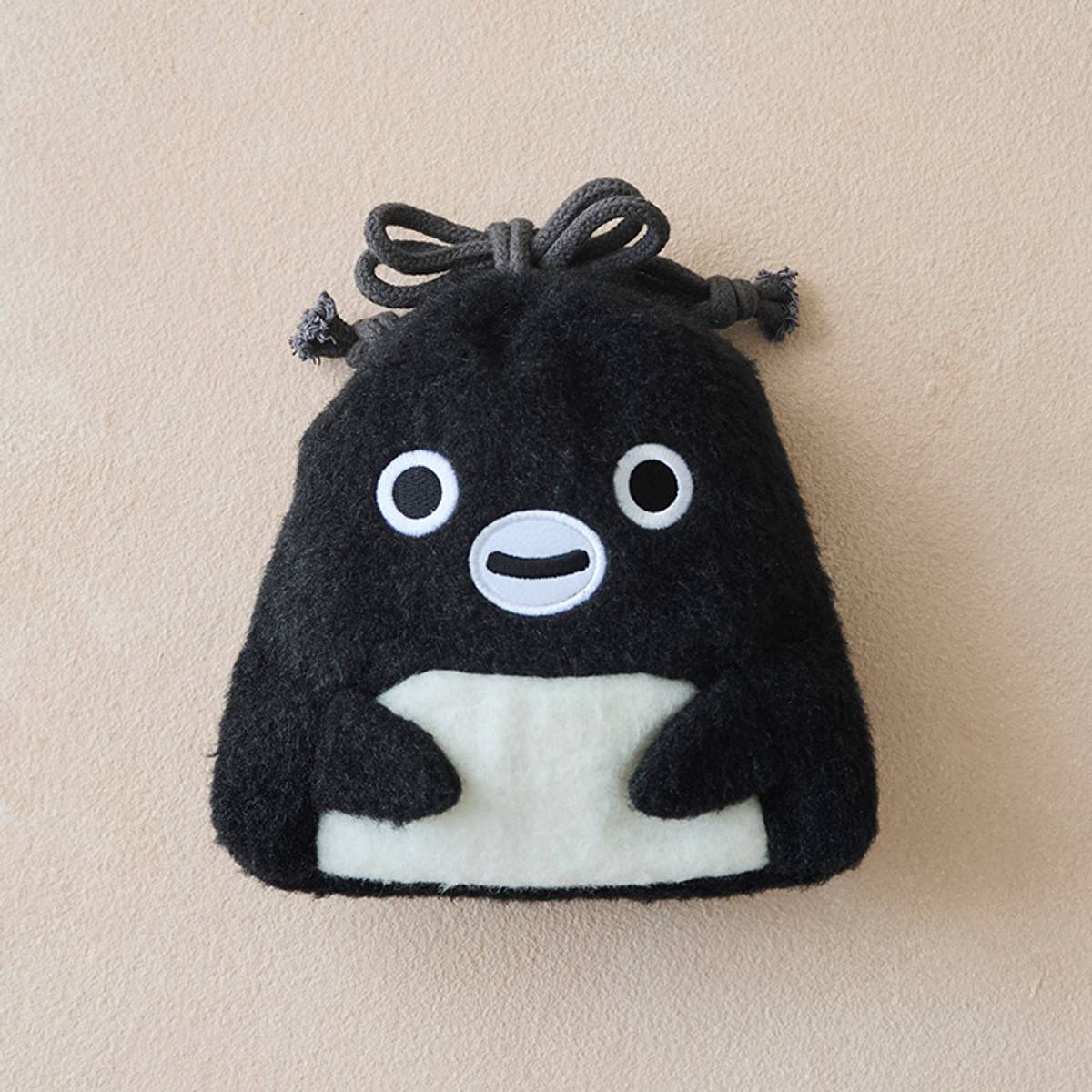 A fluffy black penguin-shaped drawstring pouch with white eyes, mouth, and belly, on a beige background.