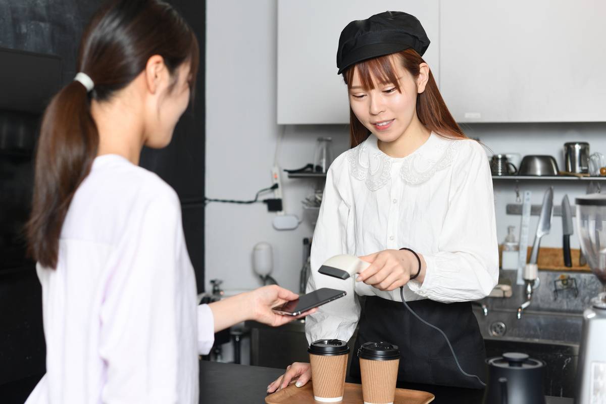 A barista scans a customer's smartphone for mobile payment at a cafe.
