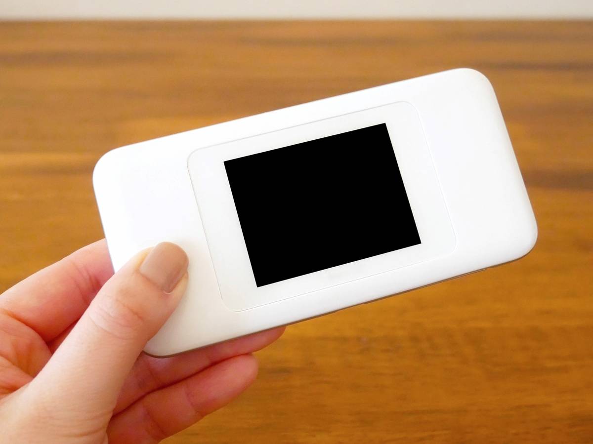 A hand holds a white mobile Wi-Fi hotspot with a black screen.