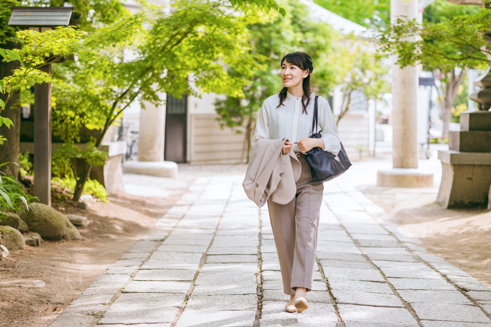 A smiling woman walks on a stone path in a serene temple garden.