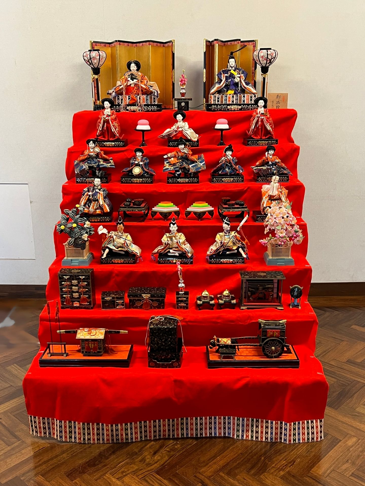 A traditional Hina Matsuri display with a tiered red stand featuring Emperor and Empress dolls at the top