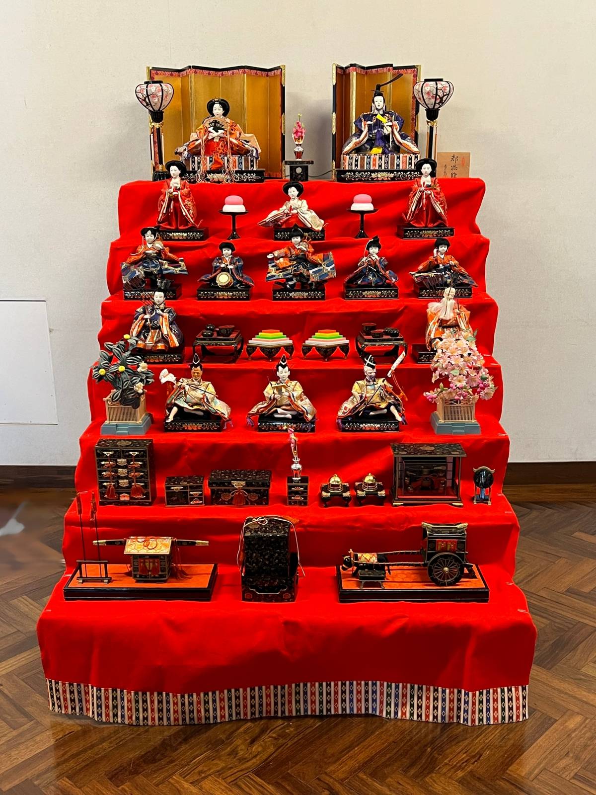 A traditional Hina Matsuri display with a tiered red stand featuring Emperor and Empress dolls at the top