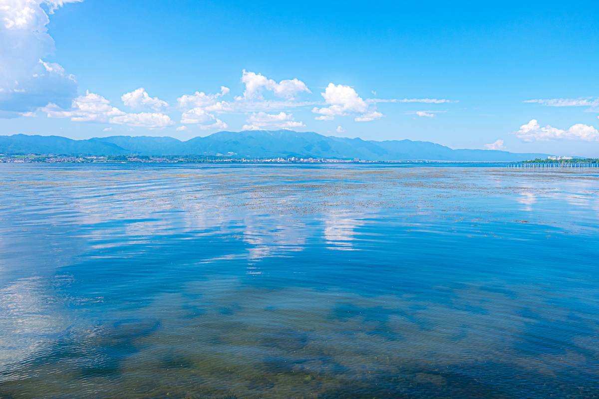A calm blue lake reflects the sky, with distant mountains and a town on the horizon.