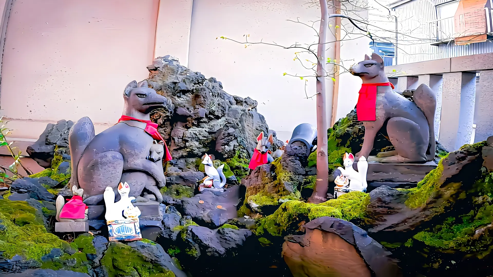Two large grey fox statues with red scarves, surrounded by smaller fox statues and moss-covered rocks.