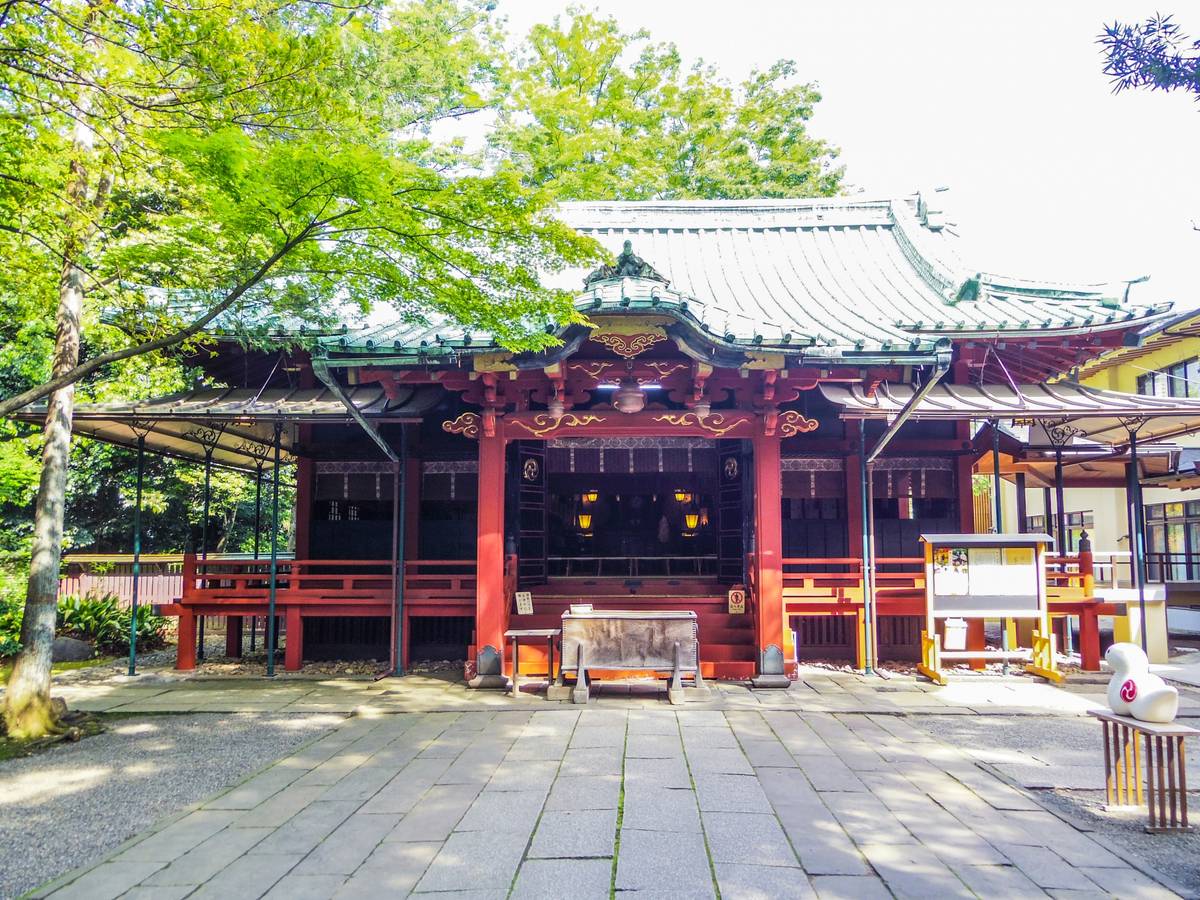 Traditional Japanese temple building with red and black accents and a green roof, surrounded by trees.