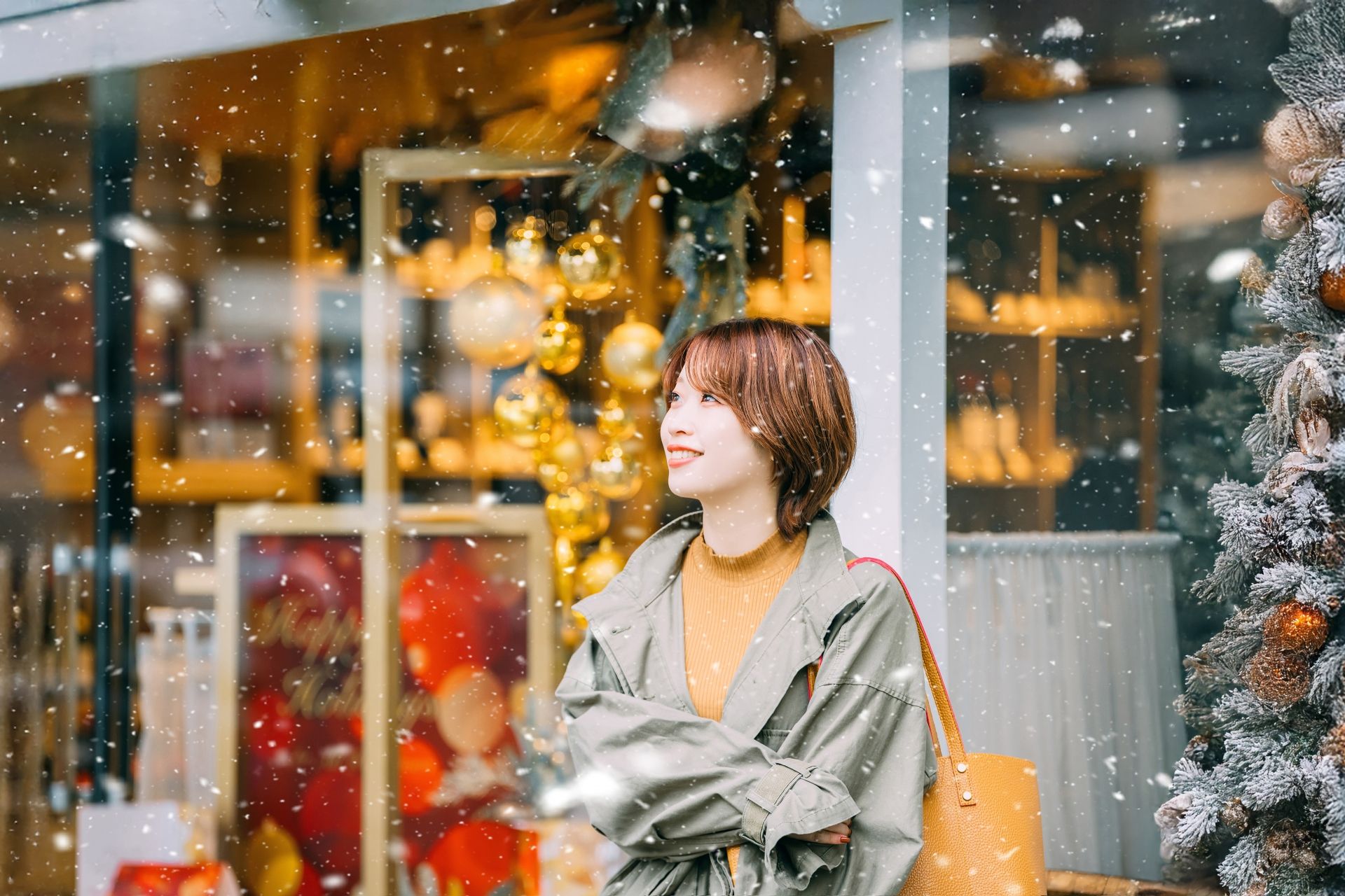 Smiling woman in a winter coat outside a festively decorated shop with falling snow.