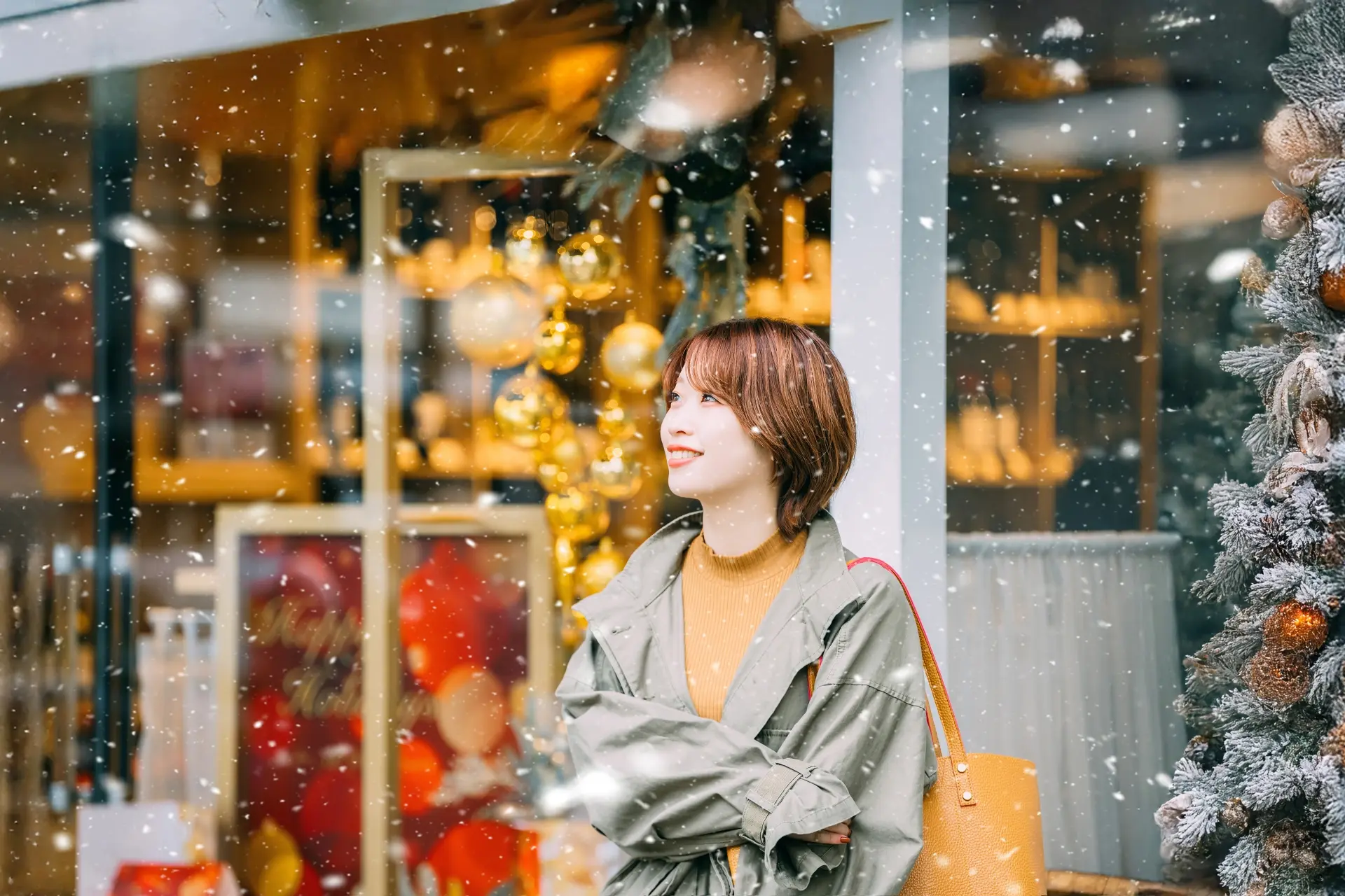 Smiling woman in a winter coat outside a festively decorated shop with falling snow.