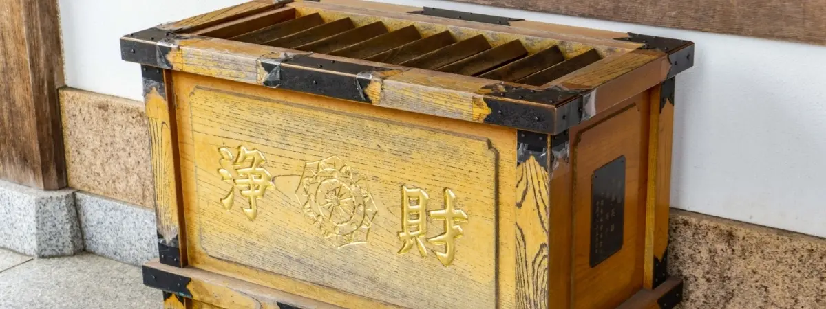 A wooden Japanese offering box with golden characters.