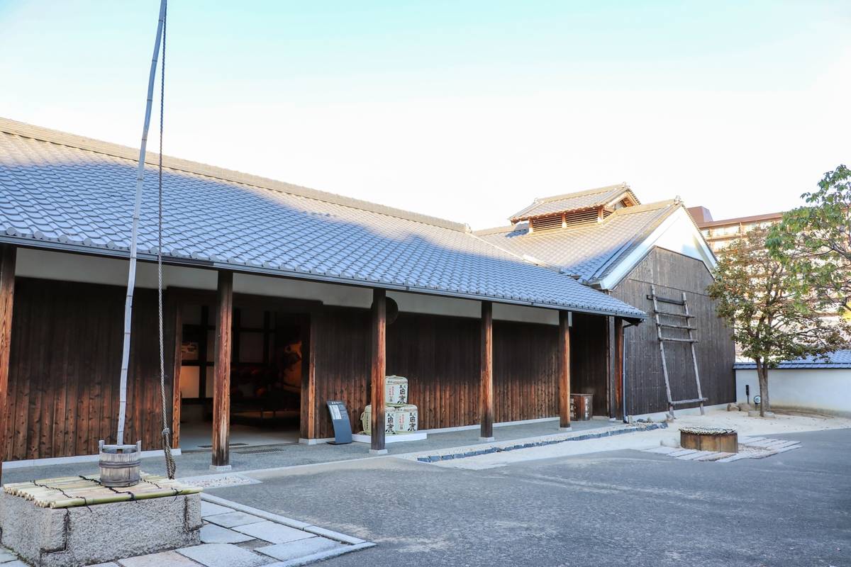 Traditional Japanese building with dark wood and a gray tiled roof, a well with a bucket and pole in the foreground.