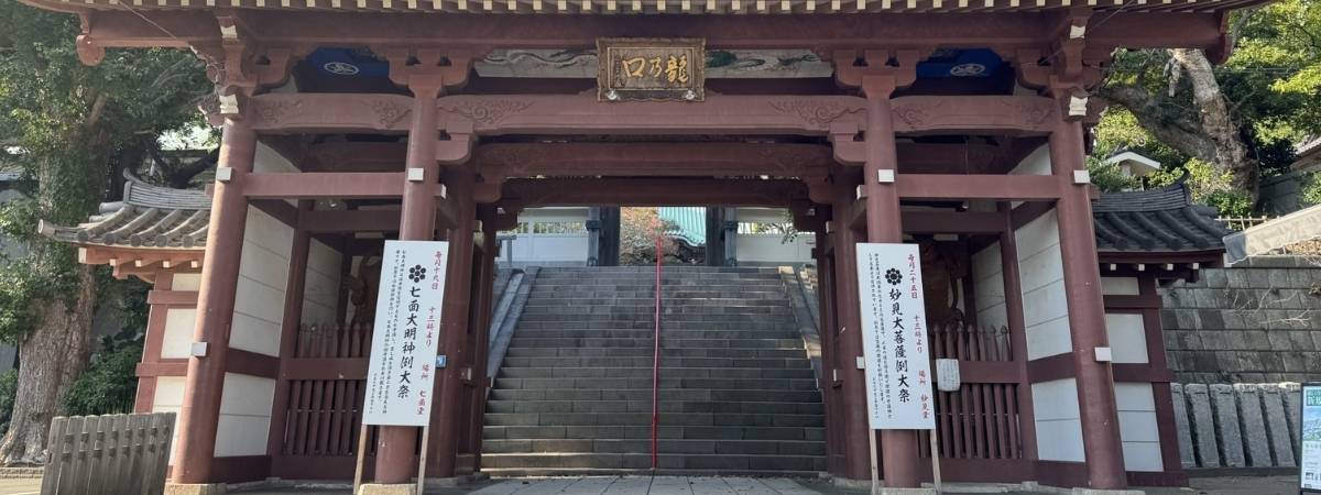 A traditional Japanese temple gate made of reddish-brown wood, with stone steps leading through it and up.