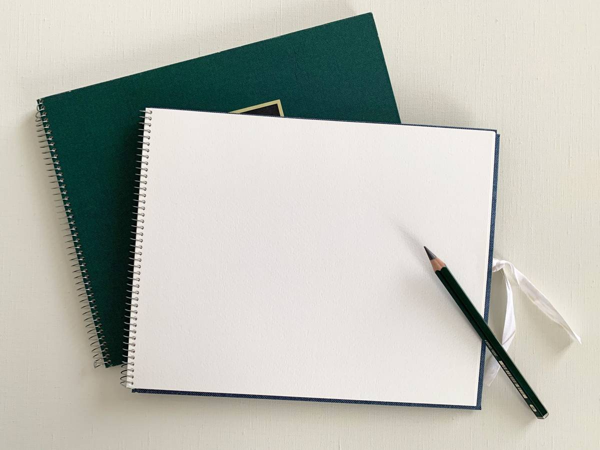 Two spiral-bound notebooks, one open to a blank page with a pencil.