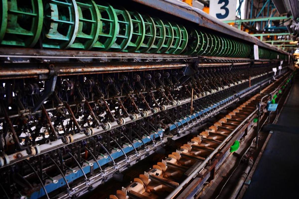 A long industrial textile spinning machine with green rotors and many spindles.