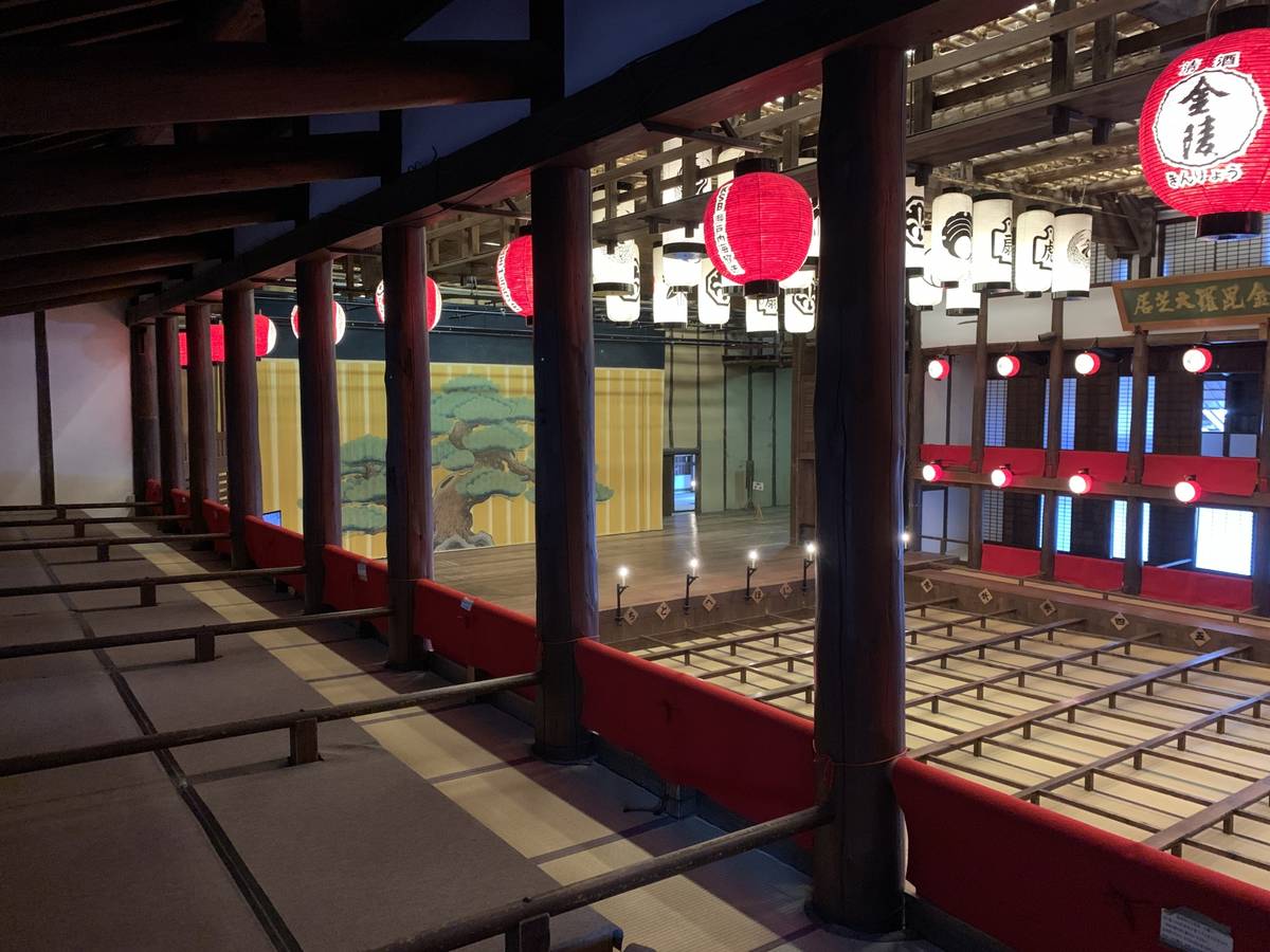 Traditional Japanese theater interior featuring a stage with a tree backdrop and many hanging red and white lanterns.