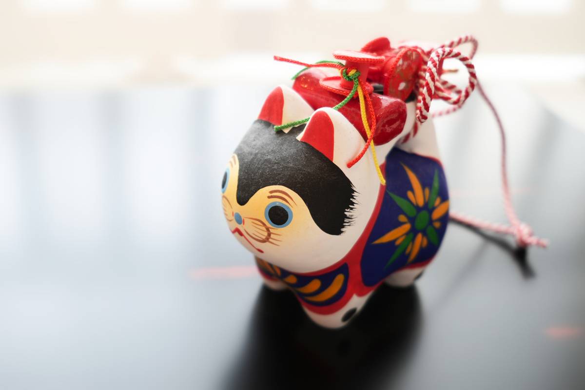 A white, black, red, and blue painted ceramic cat figure with colorful cords.