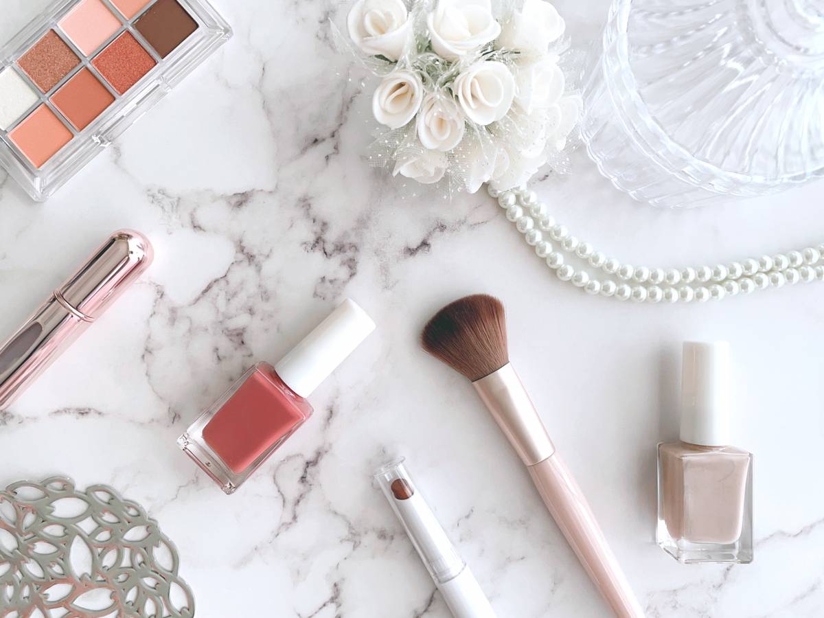 Makeup and accessories on a white marble surface, including an eyeshadow palette, nail polish