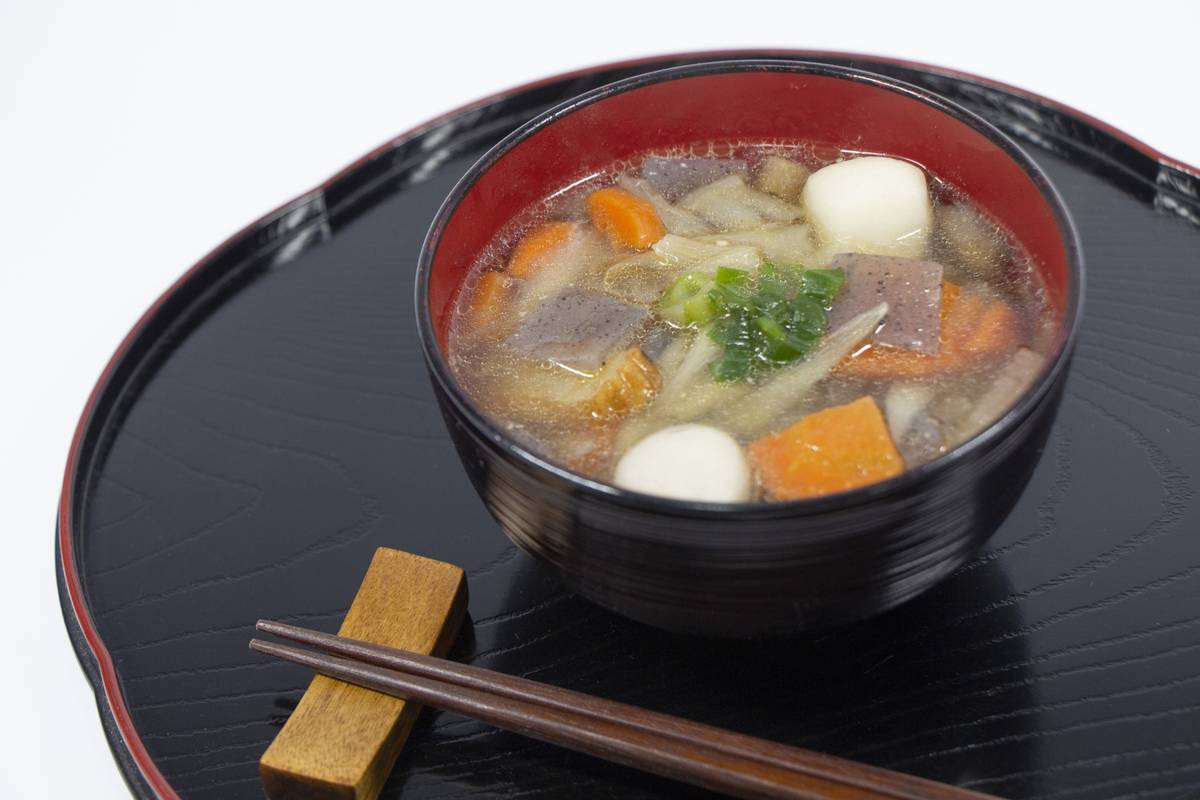 A black bowl of clear vegetable soup with white dumplings, served on a black tray with chopsticks.