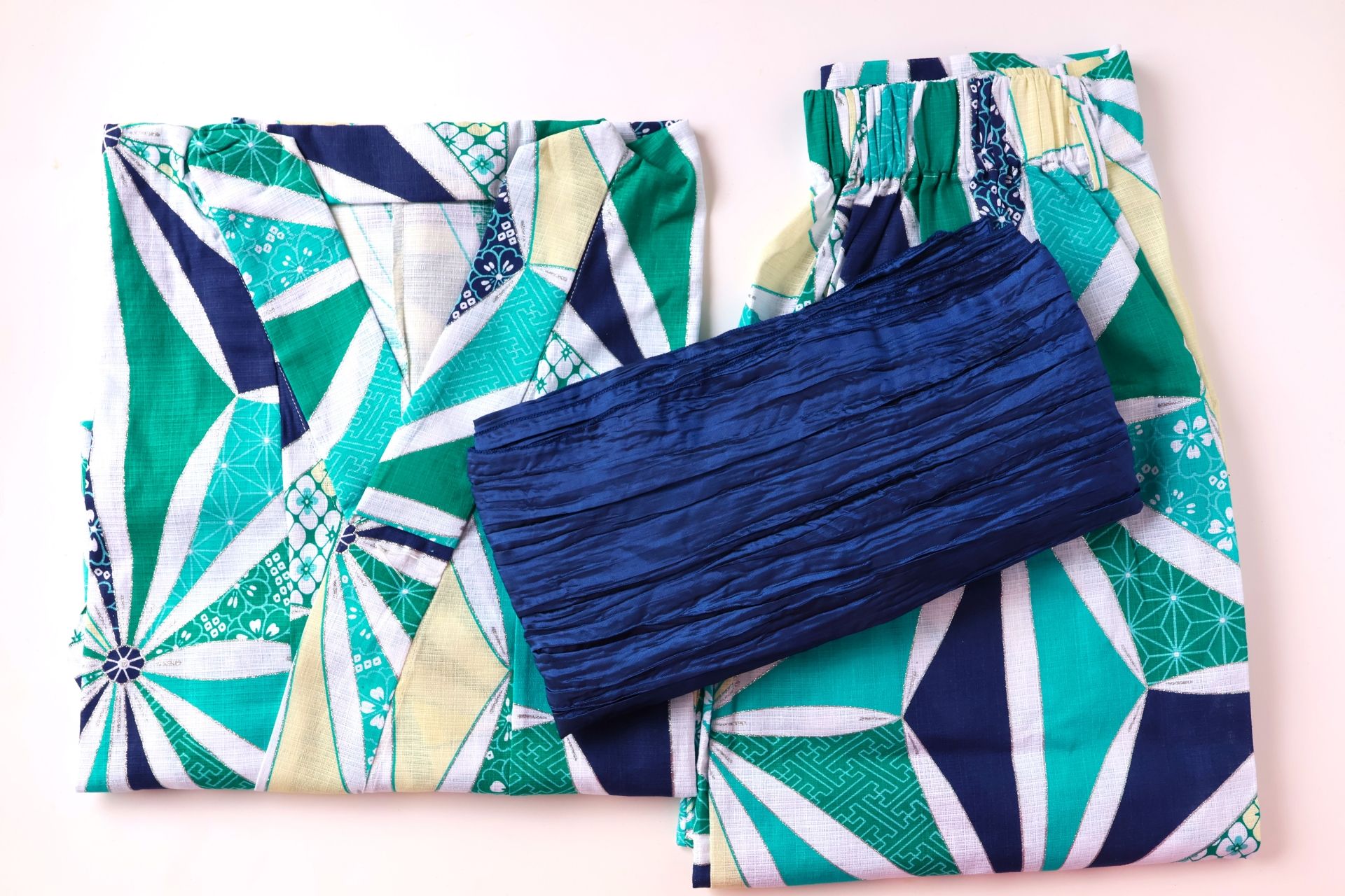 Folded yukata-style set with green, teal, navy, and white geometric patterns, and a dark blue crinkled sash.