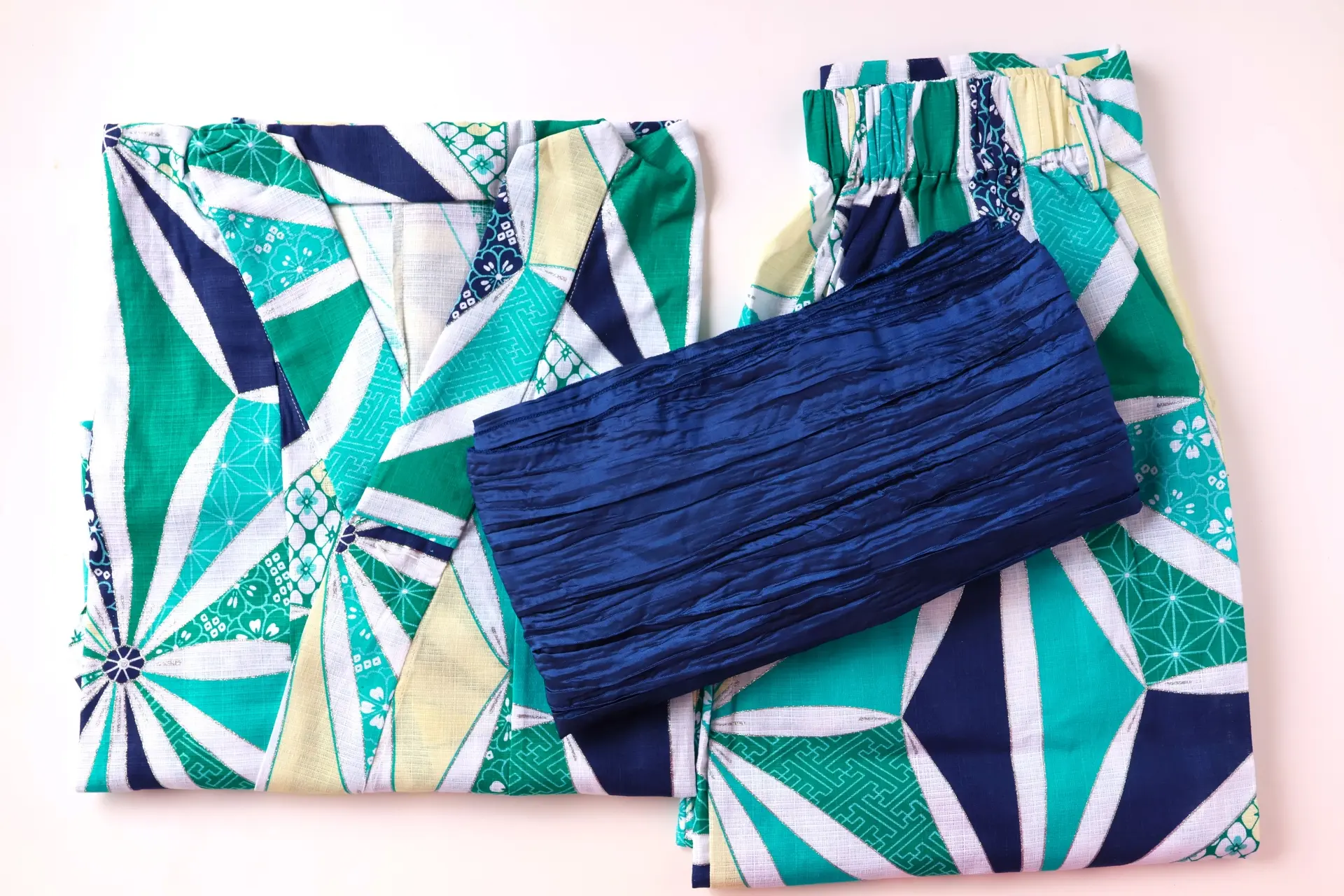 Folded yukata-style set with green, teal, navy, and white geometric patterns, and a dark blue crinkled sash.