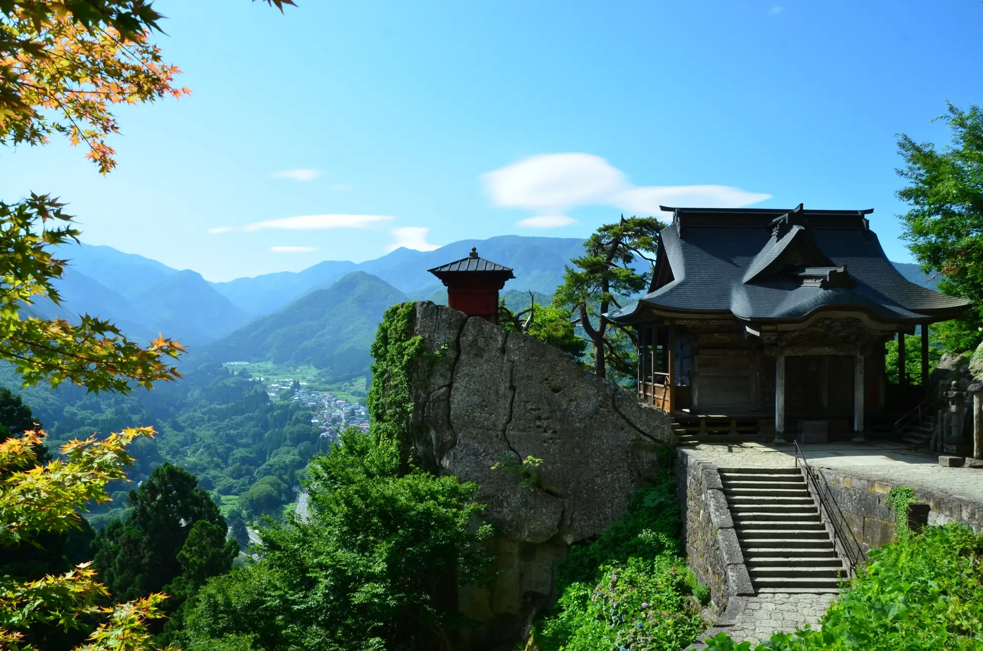 Japanese temple and red pagoda on a cliff overlooking a forested mountain valley.
