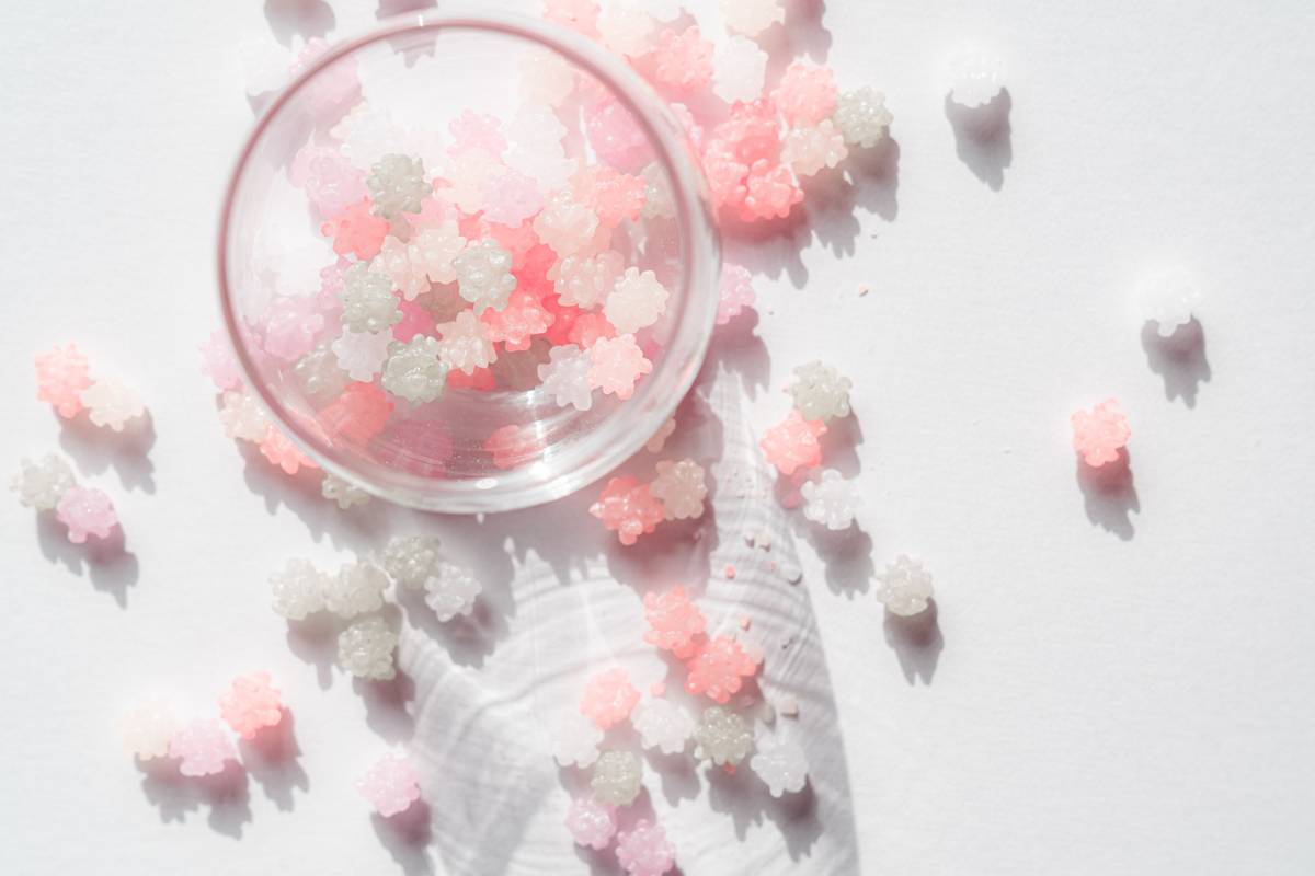 Pastel pink, peach, and white flower-shaped candies spill from an overturned glass bowl onto a white surface.