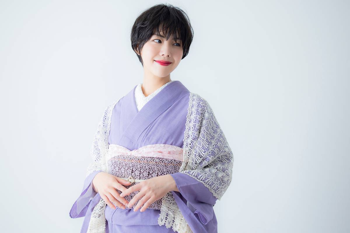 A smiling woman with short black hair wearing a light purple kimono with a white lace shawl.