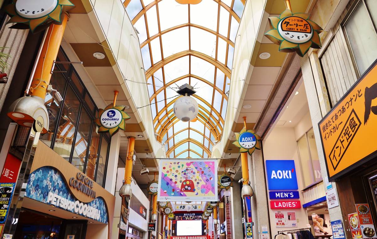 A brightly lit Japanese shopping arcade with an arched glass ceiling and numerous store signs.