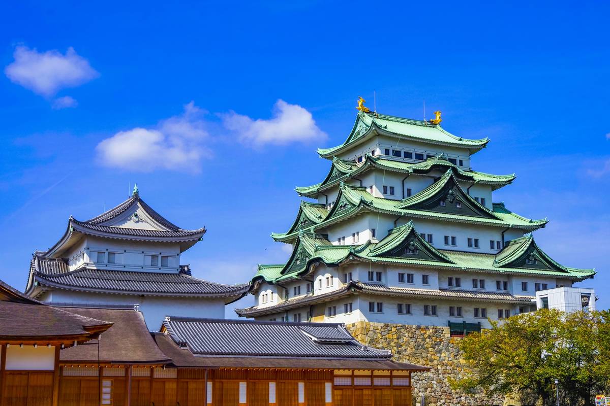 A multi-tiered Japanese castle with green roofs and traditional buildings under a bright blue sky.