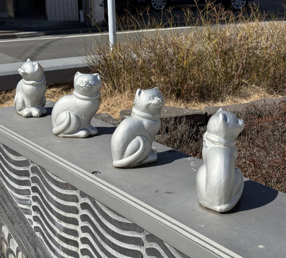 Four gray cat statues sit in a row on a ledge, one facing away.