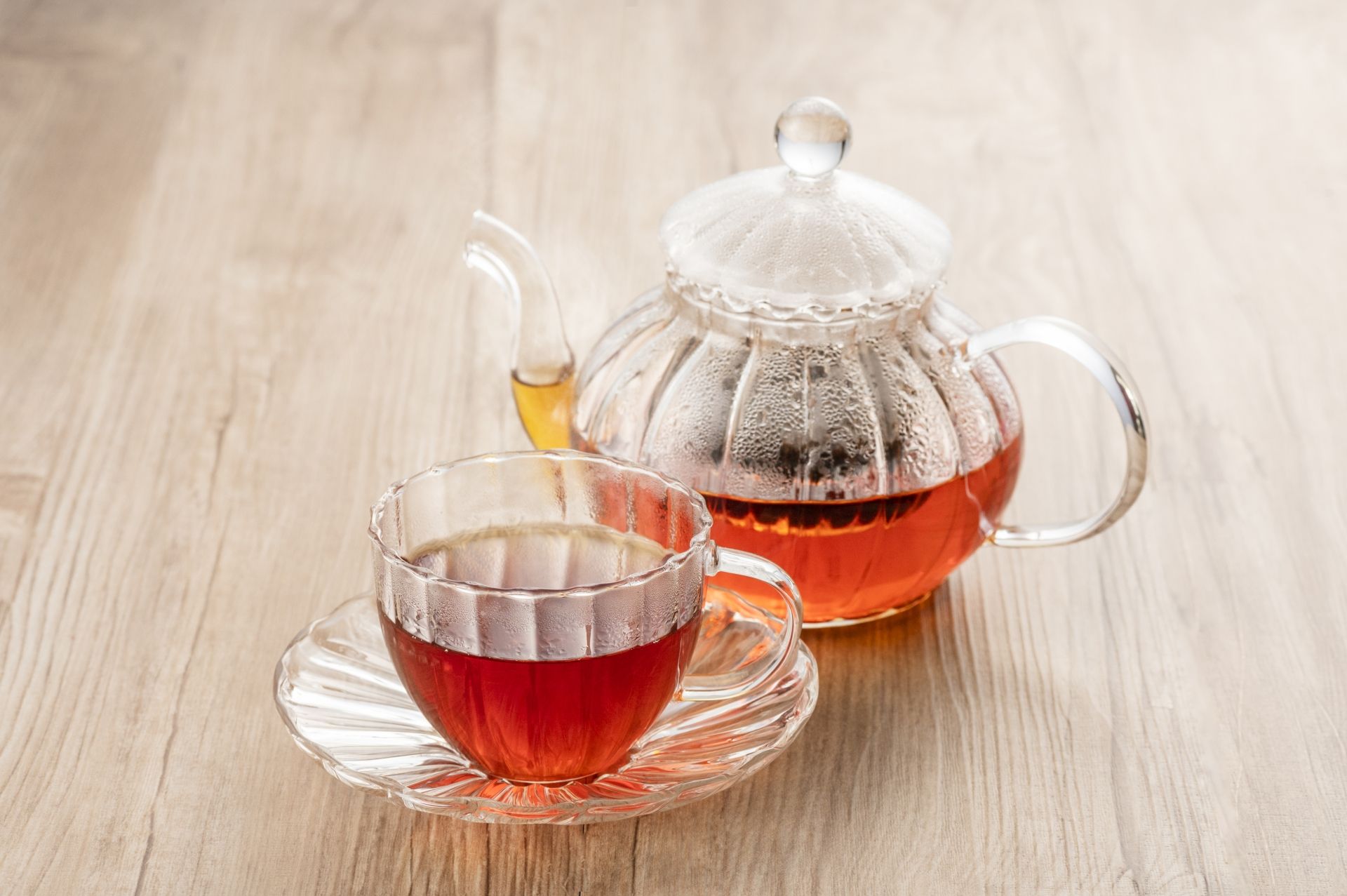 Clear glass teapot and teacup filled with red tea on a wooden surface.