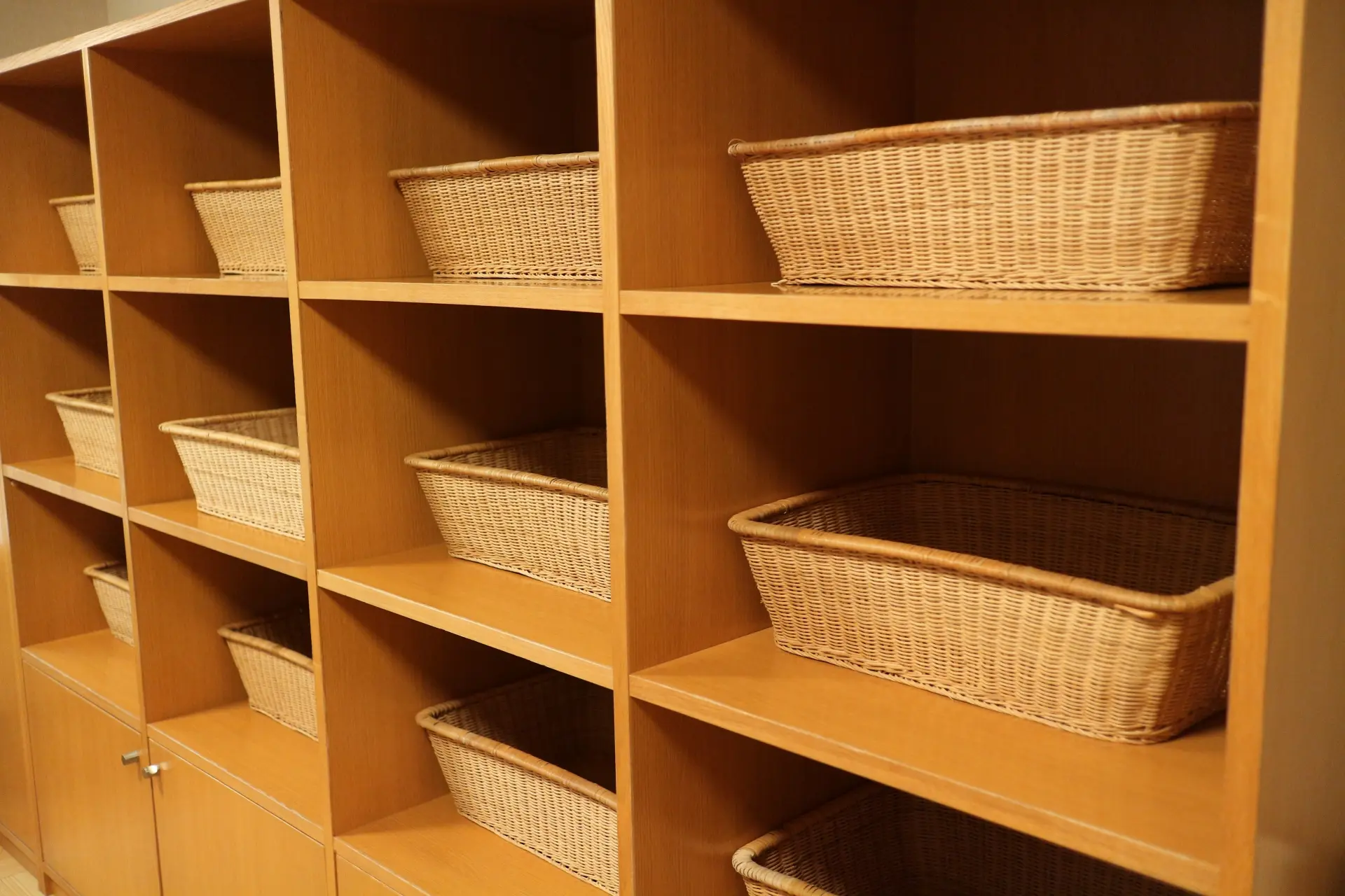 Wooden shelving unit with multiple compartments, each containing an empty woven basket.
