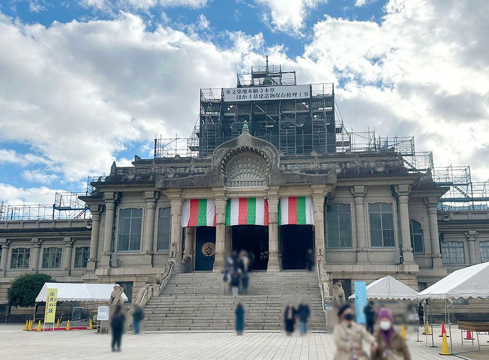 An ornate, temple-like building with scaffolding on its upper levels and red, white, and green banners