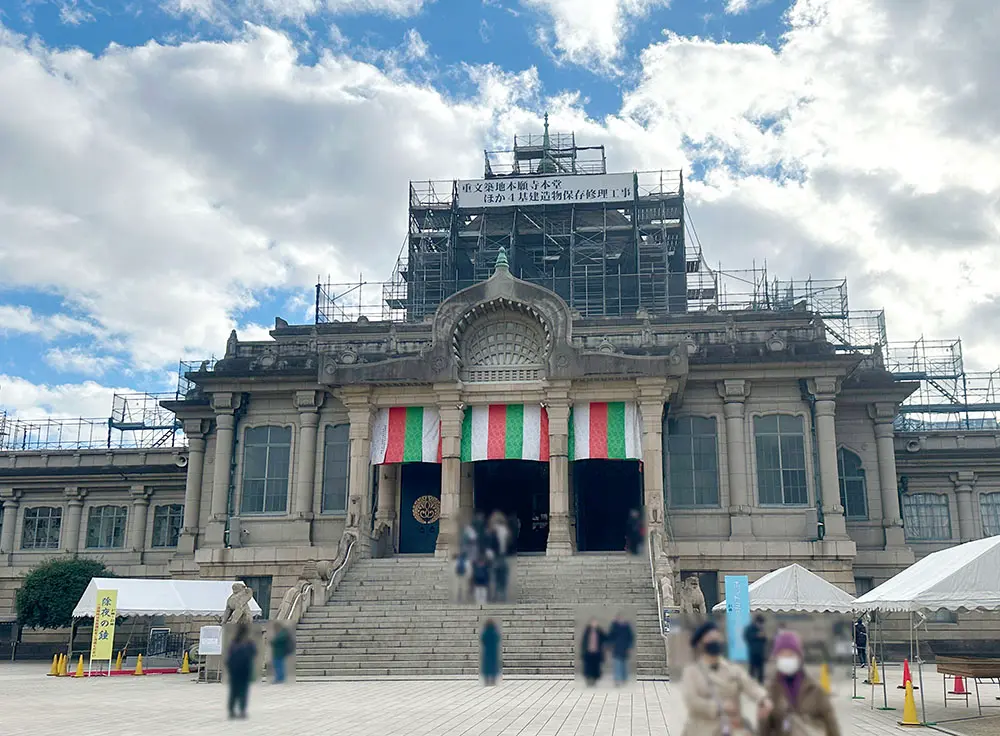 An ornate, temple-like building with scaffolding on its upper levels and red, white, and green banners