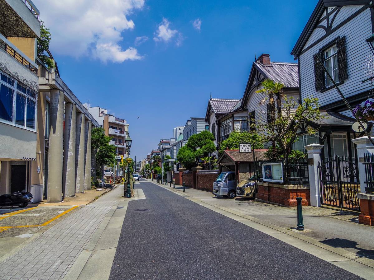 A street in Japan with historic Western-style houses on the right and modern buildings on the left, under a blue sky.