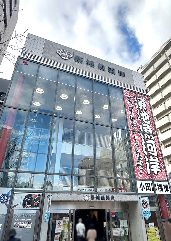 A modern multi-story glass building with "Tsukiji Uogashi" signage and a prominent red banner.
