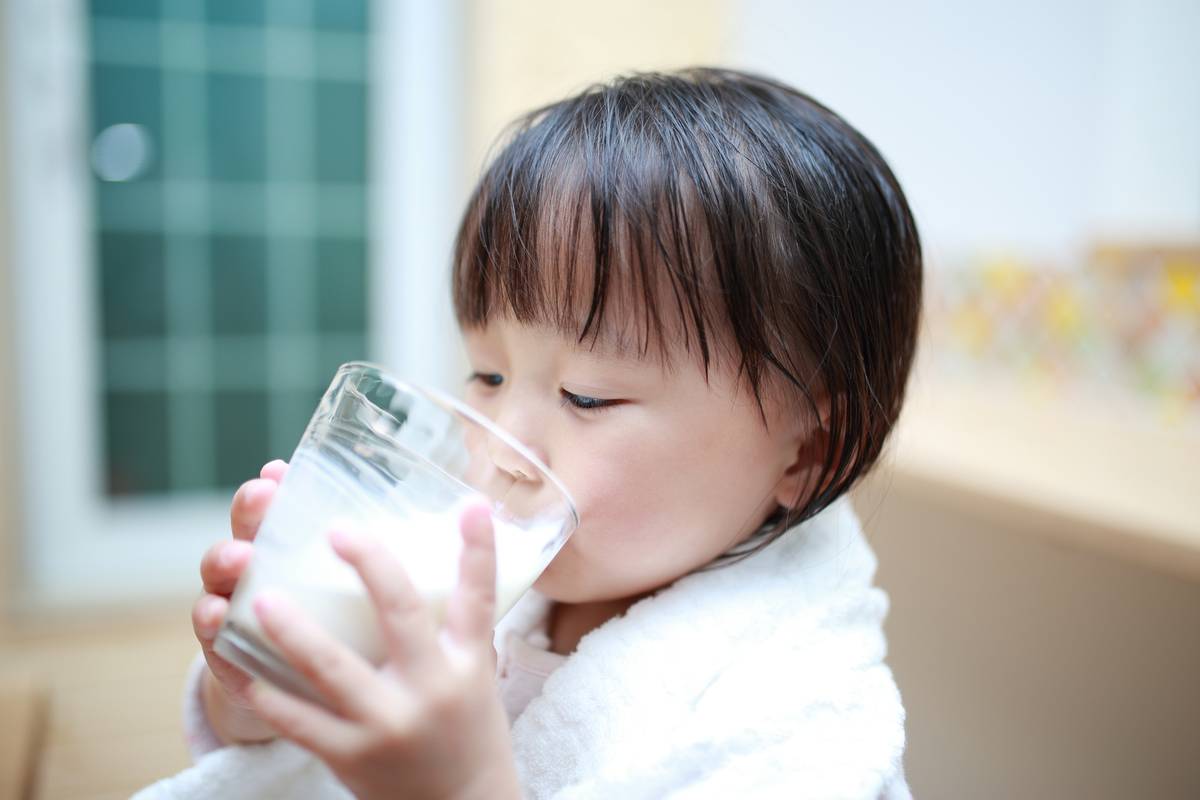 A young child in a white robe drinks milk from a glass.