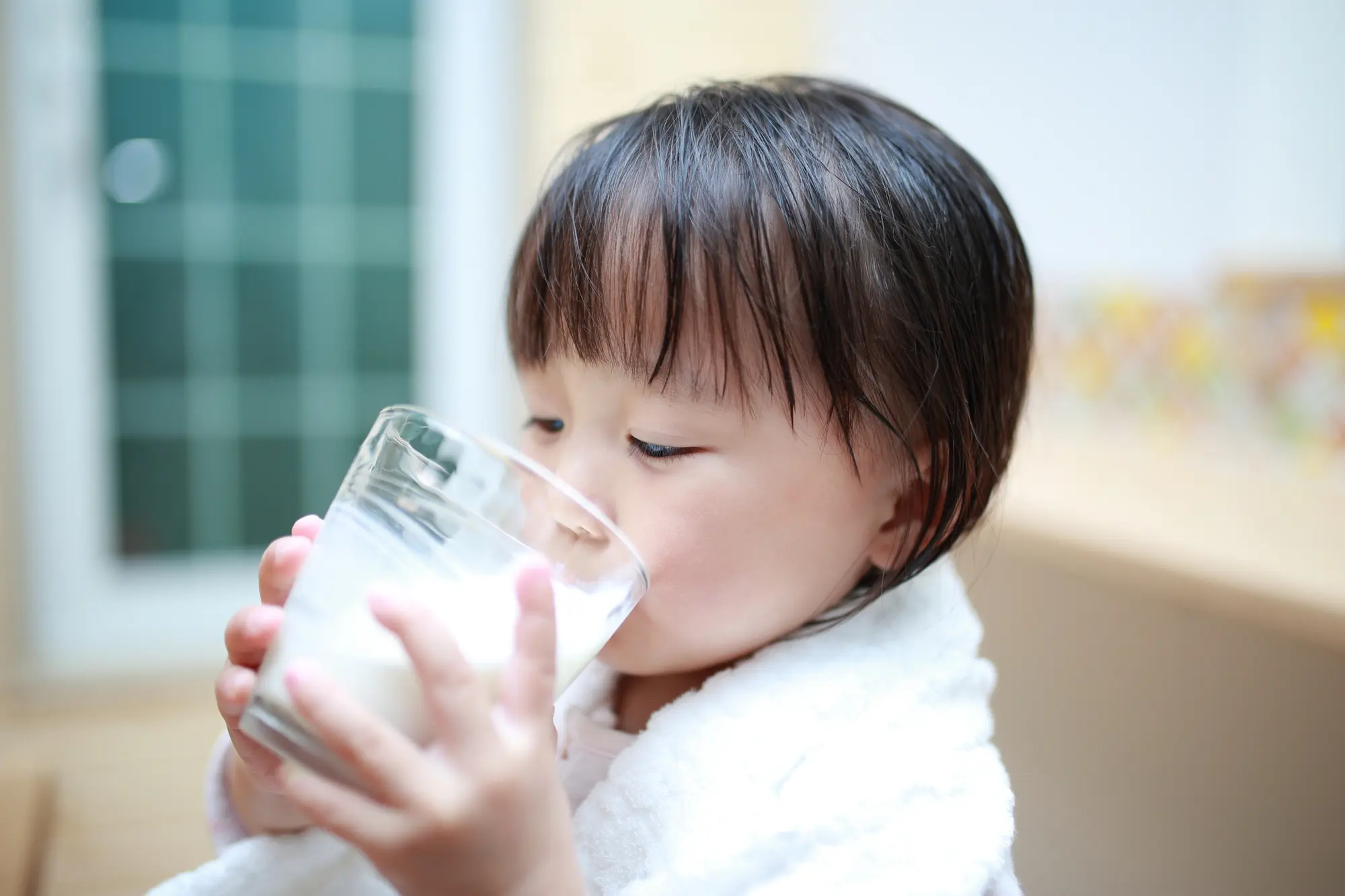 A young child in a white robe drinks milk from a glass.