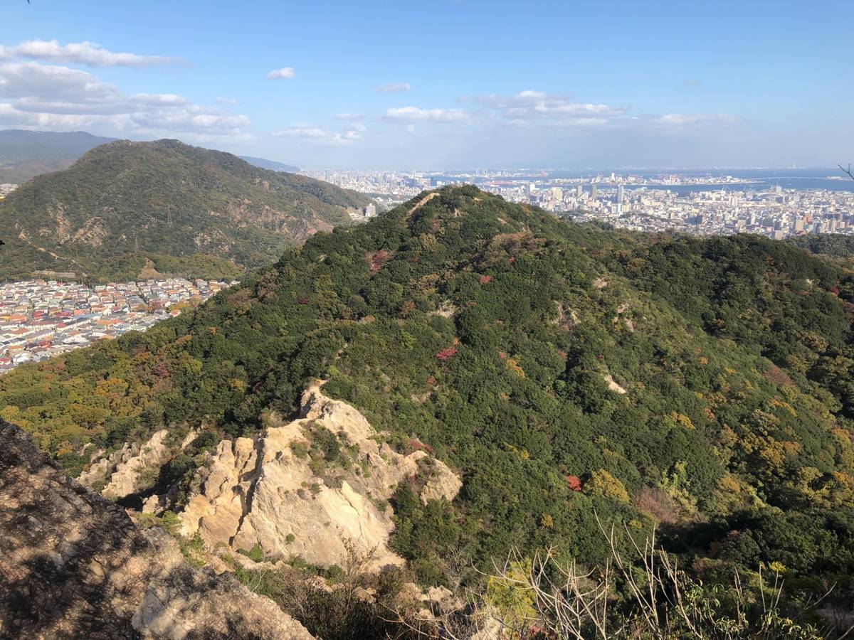 View from a rocky outcrop overlooking forested mountains, a city, and a bay under a clear blue sky.