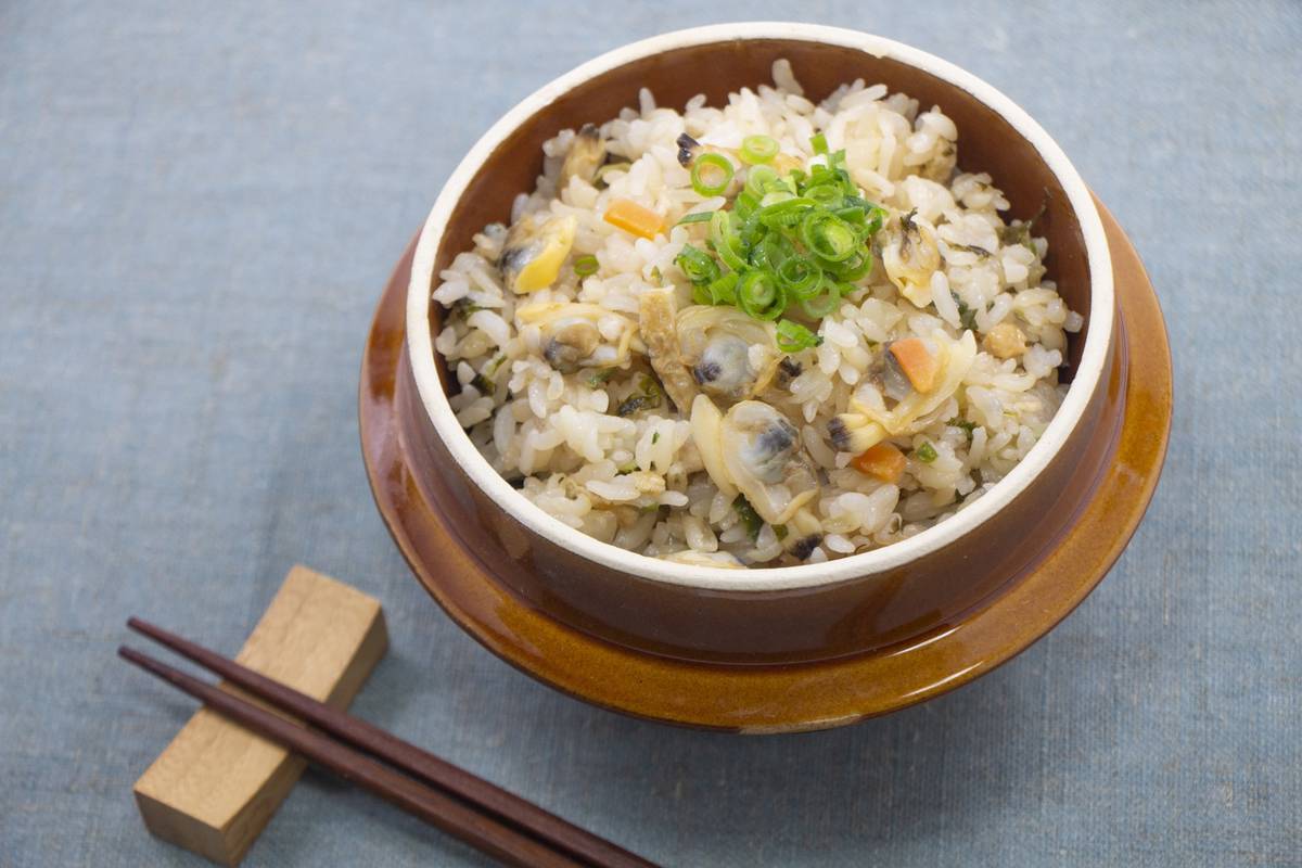 Clam rice in a brown bowl with green onion garnish and chopsticks.