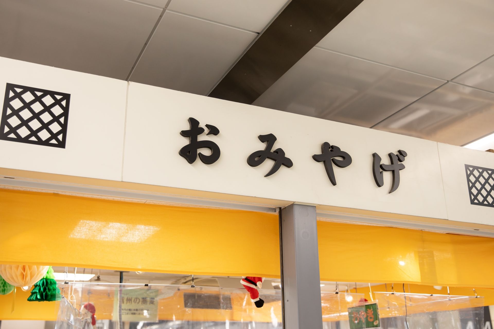 White sign with black Japanese characters "おみやげ" (omiyage), meaning souvenir, above a yellow awning.