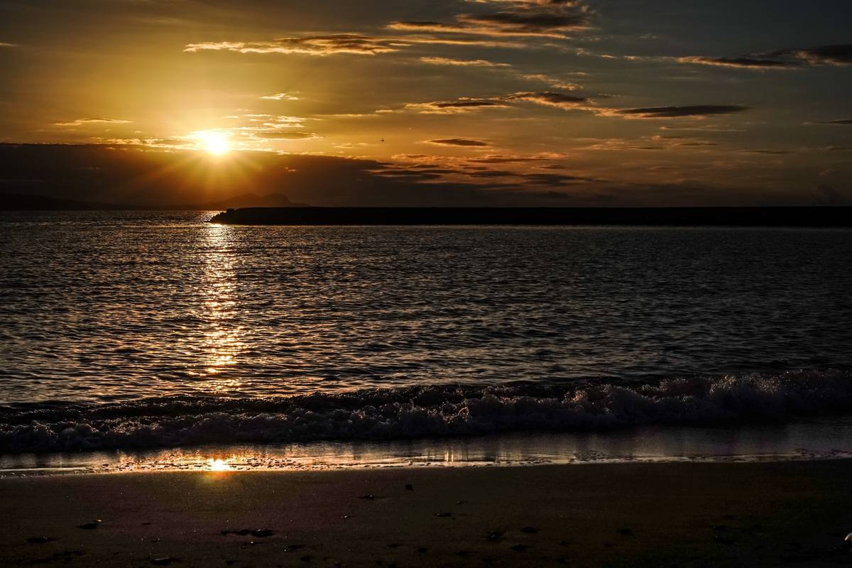 Golden sunset reflecting on water with waves on a beach.