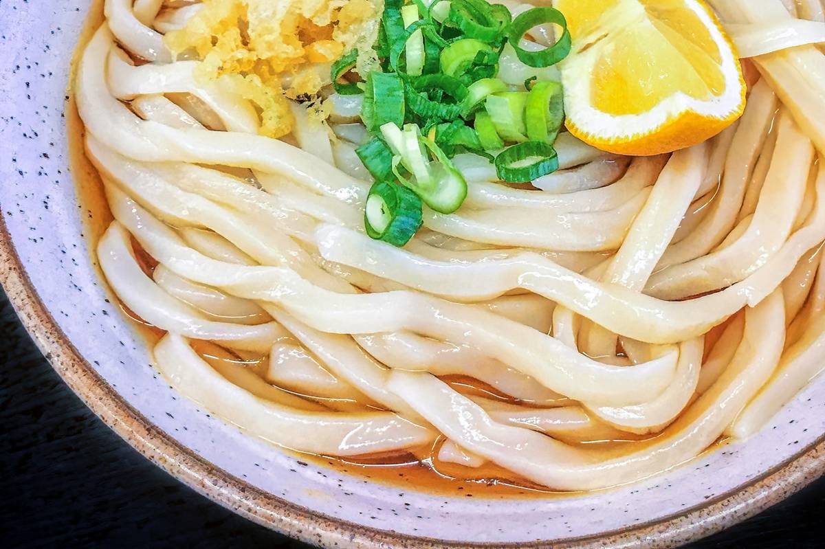 Udon noodles in broth, topped with green onions, tempura flakes, and a lemon wedge.