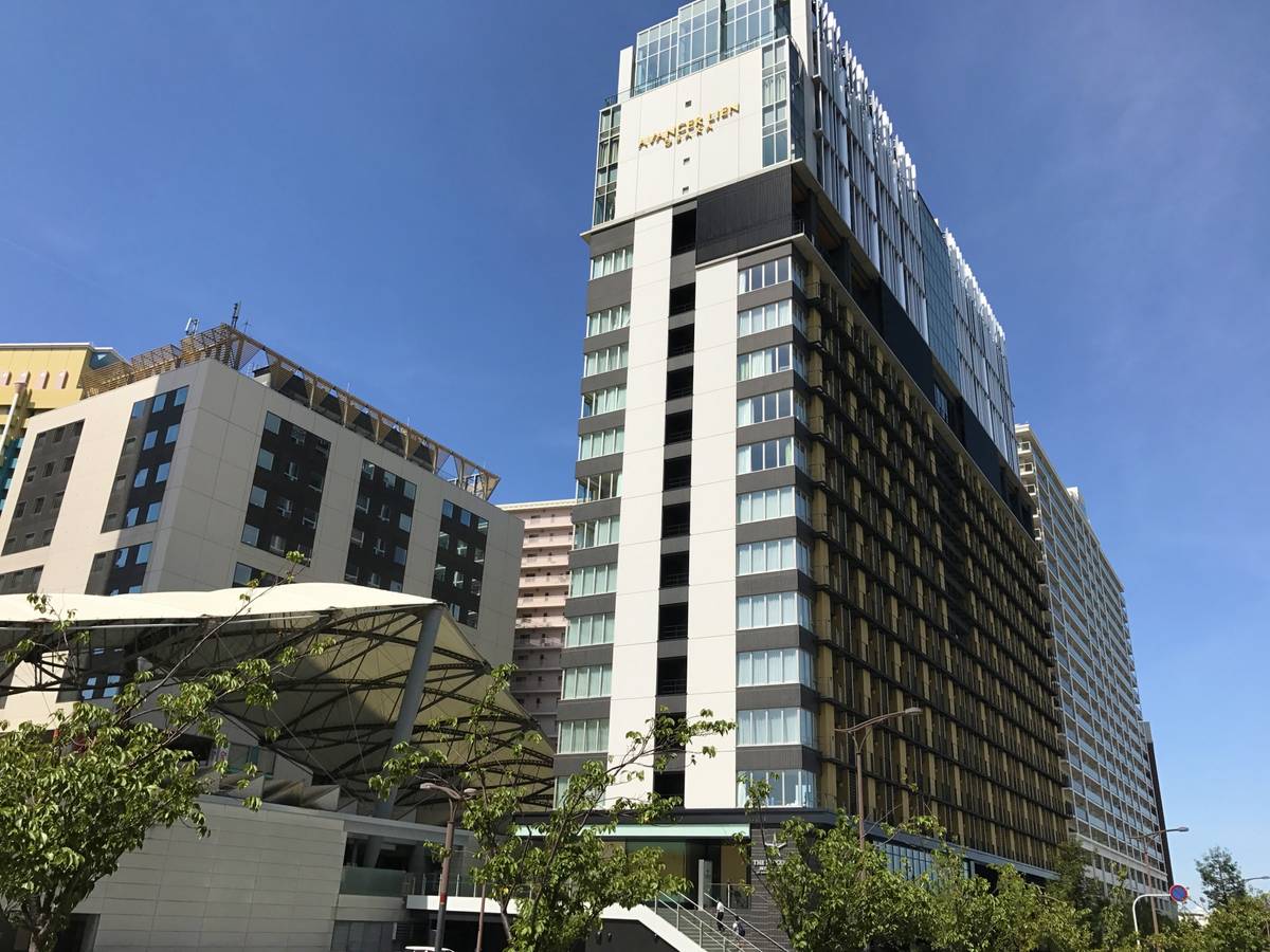 A tall modern hotel building labeled "APANESE LIEN HOTEL" stands next to a white angular building under a clear blue sky.